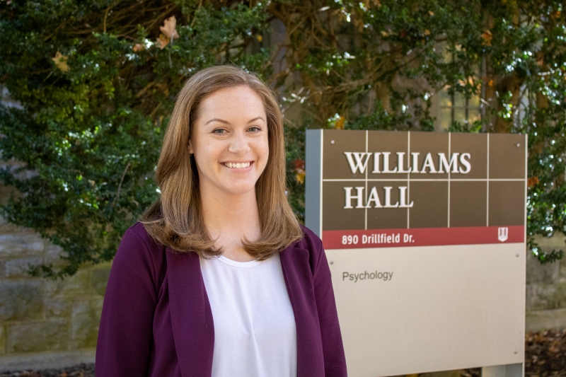 Meagan Brem stands outside in front of the Williams Hall building sign on Virginia Tech's campus wearing a white shirt and purple blazer jacket.